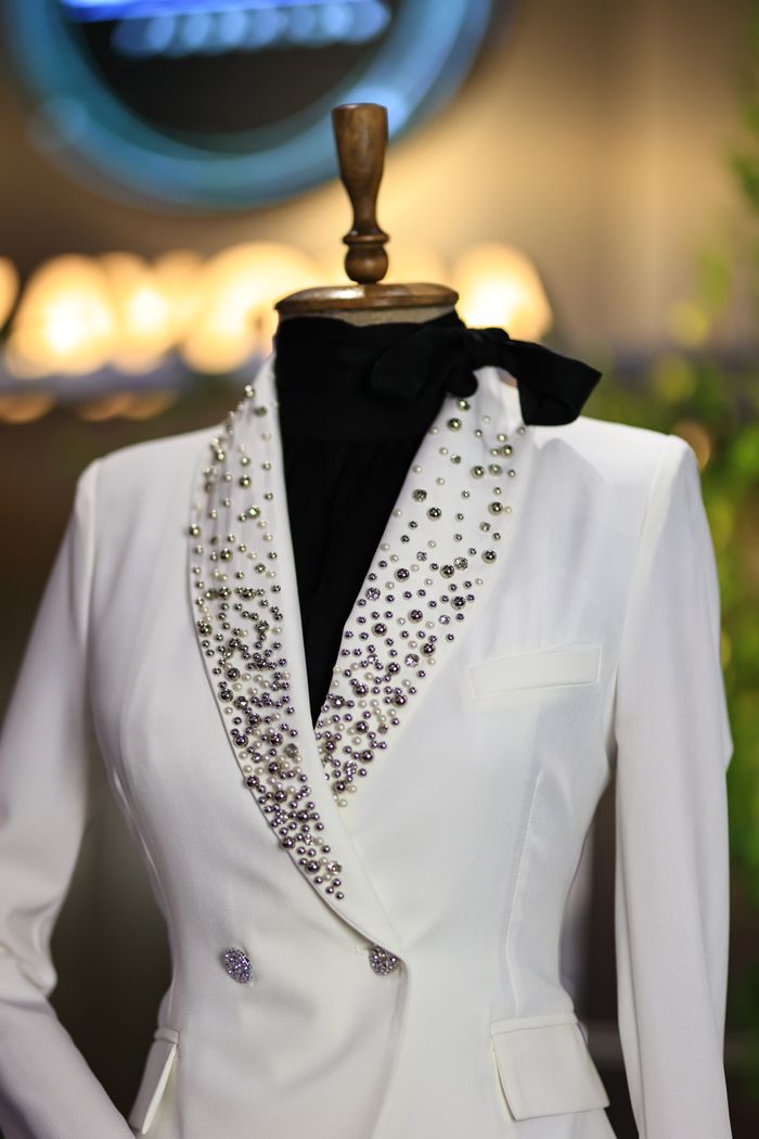 gallery-3 Luxurious white blazer adorned with sparkling jewels displayed on a mannequin in a boutique.